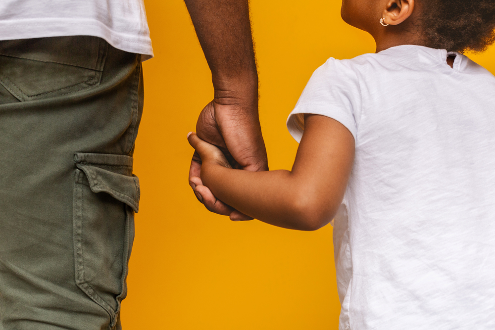 Father and toddler daughter holding hands, yellow background - child support arrears