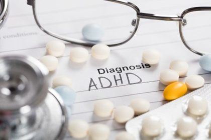 A pair of glasses, stethoscope, and scattered white pills lay on top of a page that says "Diagnosis ADHD"