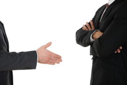 A person on the left holds out their hand for a handshake while another person on the right stands with their arms crossed.