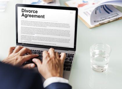 A laptop with a divorce agreement on the screen sits on a desk with paperwork
