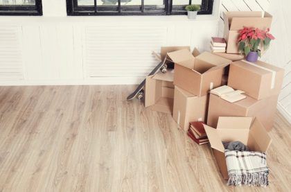 Moving boxes sit on a wood floor against a white wall with black-trimmed windows.