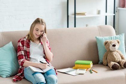 teenage girl sitting on a couch talking on a cell phone