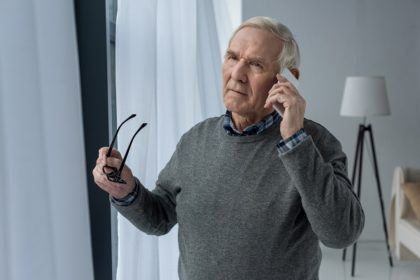 an older man holds his glasses while talking on a cell phone