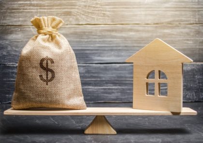 Picture of a Scale with a money bag on one end, and a house on the other