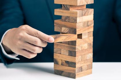 A man in a suit jacket pulls a block out of a Jenga stack