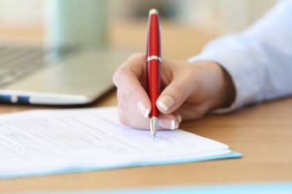 A woman signing a document with a red pen