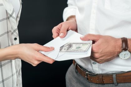 A man on the right hands an envelope with a 100-dollar bill in it to a woman on the left