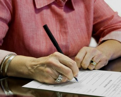 A woman in a pink shirt signs a legal document.