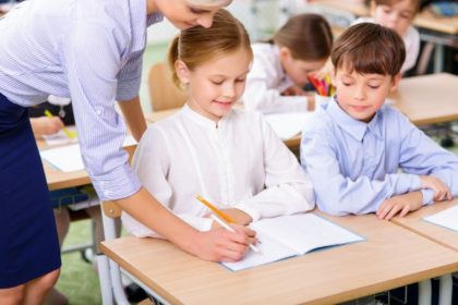 A teacher helps a smiling young girl with her work in class.