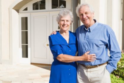 An older couple posing in front of their house.