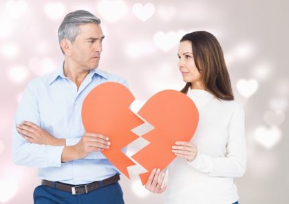 An older man and woman hold up two separate pieces of a broken paper heart.
