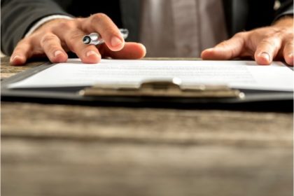 A man with hands on top of legal documents, a pen tucked under one of his fingers.