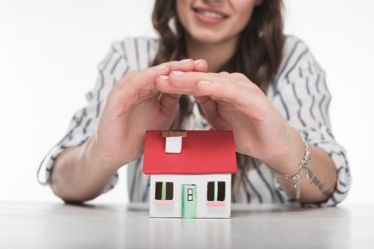 a smiling woman holds her hands over a small model home