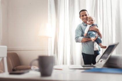 A father holds his young child in front of him while smiling at the candle.