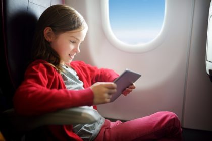 a young girl on an airplane watches a video on an electronic device