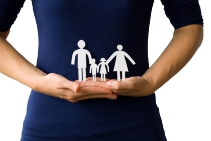 A woman in a blue shirt holds a white paper cutout family on top of her hands.