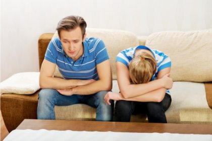 A man and woman sit on a couch, upset.