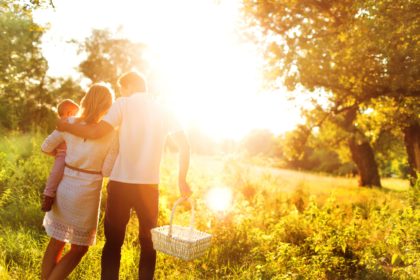 A family walking together through a field toward the setting sun.