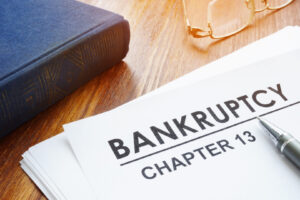 close up of papers that read bankruptcy, chapter 13 on desk along with book and reading glasses