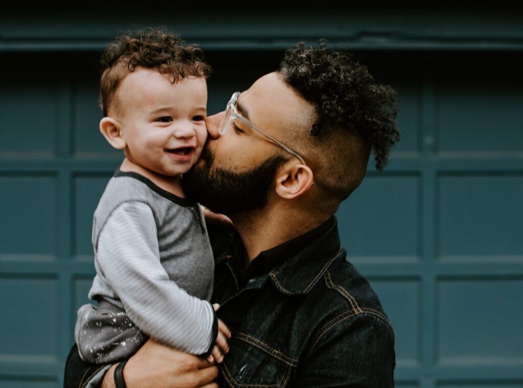 Dad holding toddler and kissing him on the cheek