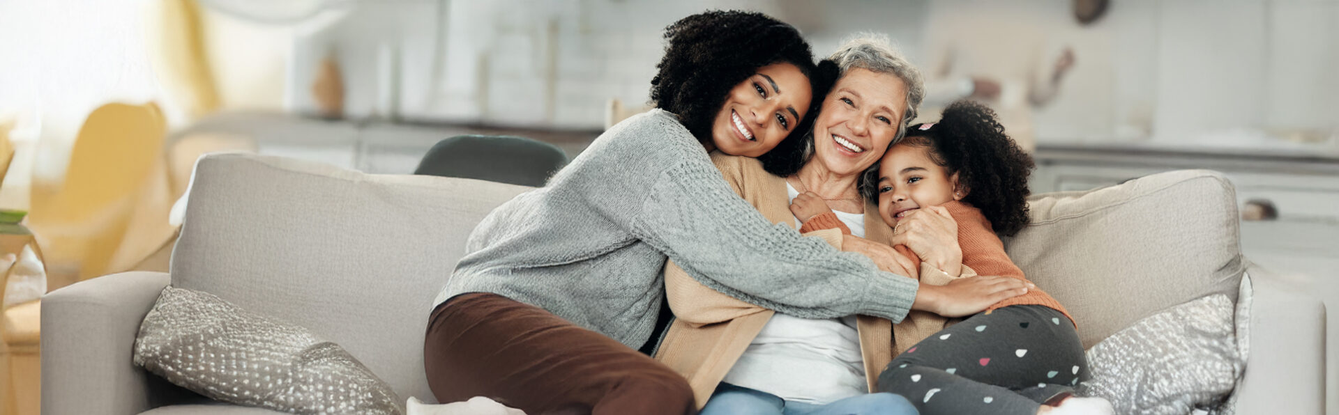 Mother with daughter and her mother in living room on couch smiling and cuddling together