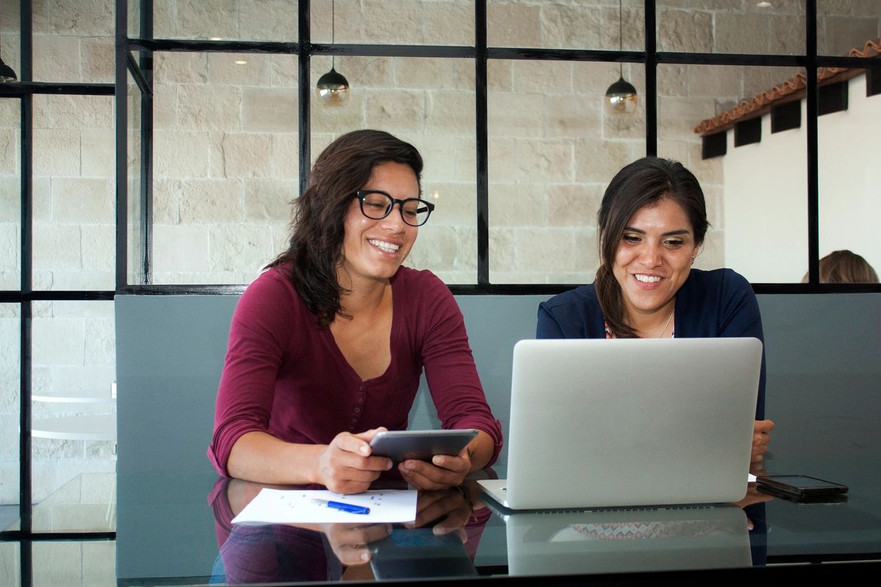 Two young women working in a public setting infront of a laptop