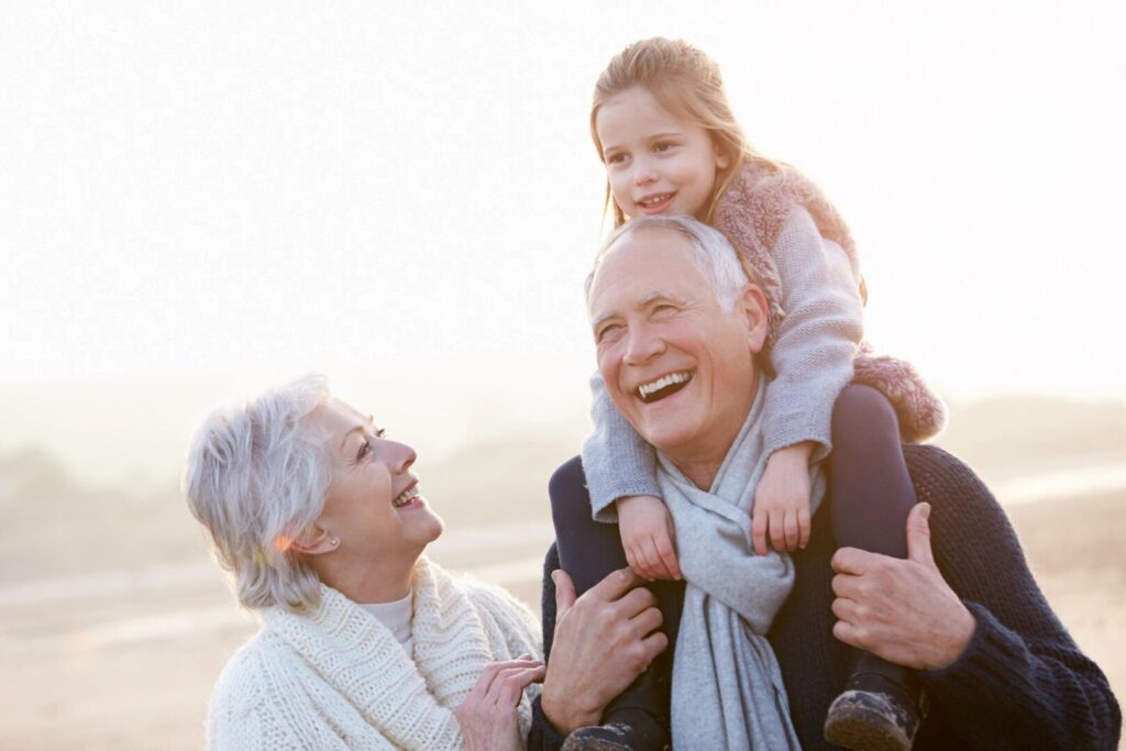 grandparents playing with grand daughter who is seated on grandpa's shoulders