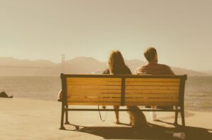 couple seated on bench looking toward San Francisco bay bridge but looking in opposite directions