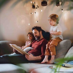 dad sitting on a couch with his 2 young kid reading a book